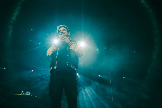 Ismo Leikola on stage under blue and white spotlights, photographed by MacKintosh Photo.