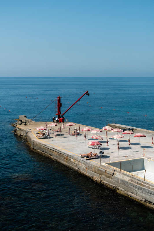 Blue Ligurian Sea and a stone sunbathing platform with striped umbrellas in Genova, Italy